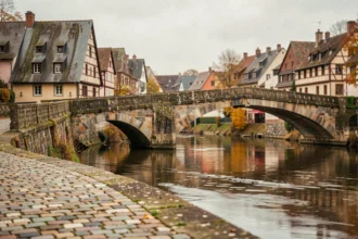 Pont historique en pierre enjambant la Sarre à Sarralbe avec architecture lorraine traditionnelle en arrière-plan à l'automne