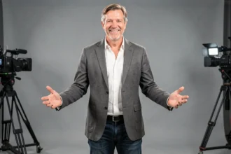 Animateur français de grande taille debout en studio de télévision, posture confiante illustrant la taille de Vincent Lagaf
